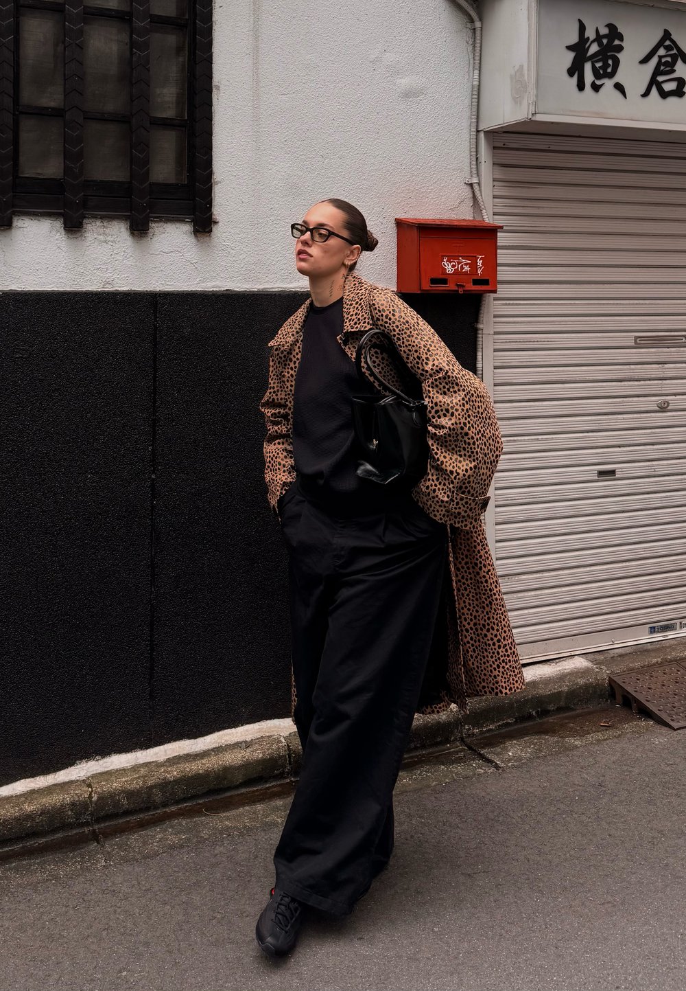 Leopárdmintás ballonkabát fekete pulóverrel, fekete bőszárú nadrággal és strukturált fekete kézitáskával párosítva. Kaszualis városi környezet.