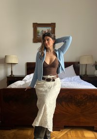 Cardigã canelado azul claro, blusa justa castanha, saia branca com padrão xadrez, grande fivela de cinto prateada, botas castanhas até ao joelho.