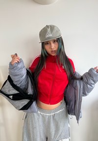 Punainen vetoketjullinen urheilutakki, harmaa toppatakki verkkotaskulla, harmaat kuluneet collegehousut ja harmaa Adidas-logolla varustettu lippalakki.