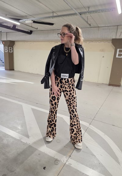 Camiseta negra corta con una etiqueta, combinada con pantalones de campana de estampado de leopardo. El conjunto incluye una chaqueta de cuero y zapatillas blancas.
