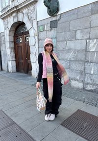 Veste matelassée rose, haut noir et pantalon cargo noir ample. Écharpe tissée rose et orange. Porte un sac à main à motifs multicolores.