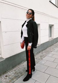 Fekete bőrkabát, fehér garbó, fekete nadrág piros oldalsó gombokkal és fekete bokacsizma. Piros clutch és kerek napszemüveg.