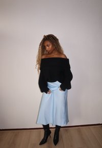 Sweater de malha preto com ombros à mostra, saia de cetim azul claro, botins pretos de salto fino. Texturas suaves, corte descontraído, mangas longas e brilho sutil.