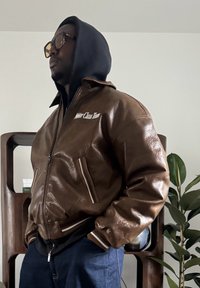 Veste aviateur en cuir marron avec fermeture éclair sur le devant, poignets et col côtelés. Présente la broderie "Motor Class Team" sur la poitrine.