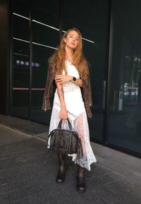 Brown leather jacket over a white top and a lace white skirt, matched with knee-high brown boots and a textured black bag.