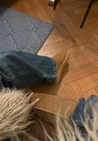 Bottines en daim marron avec une semelle texturée, associées à un jean en denim bleu. Tissu doux et duveteux partiellement visible au premier plan.