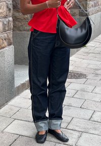Tamsiai mėlynos džinsinės kelnės su plačiomis kojomis ir apvytu hemu, derinamos su ryškiai raudona peplum palaidine ir juoda petine rankine. Lygus audinys ir kasdienis dizainas.