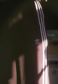 Calças de treino Adidas pretas com três riscas verticais brancas ao longo dos lados, um bolso com fecho a correr e um pequeno logótipo Adidas.