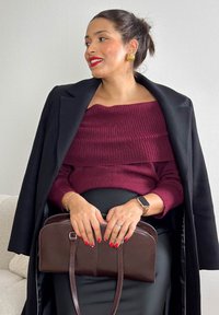 Pulover bordo cu dungi și decolteu pe umeri, palton negru și fustă lungă neagră. Geantă maro cu două mânere, textura lucioasă, design în straturi, unghii roșii.