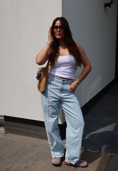 Jeans de talle alto azul claro con costuras blancas, una camiseta corta blanca y pantuflas moradas. También es visible un bolso beige con acentos morados.