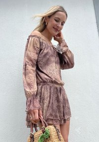 Robe marron à motif, décolletée sur les épaules, avec des manches évasées et un ourlet à volants. Tenant un sac en osier avec des accents verts. Texture lisse.