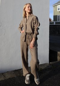 Svijetlosmeđa lanena košulja s kopčanjem na gumbe, uparena s odgovarajućim širokim hlačama. Ležerne sive tenisice s bijelim detaljima. Minimalni pribor.