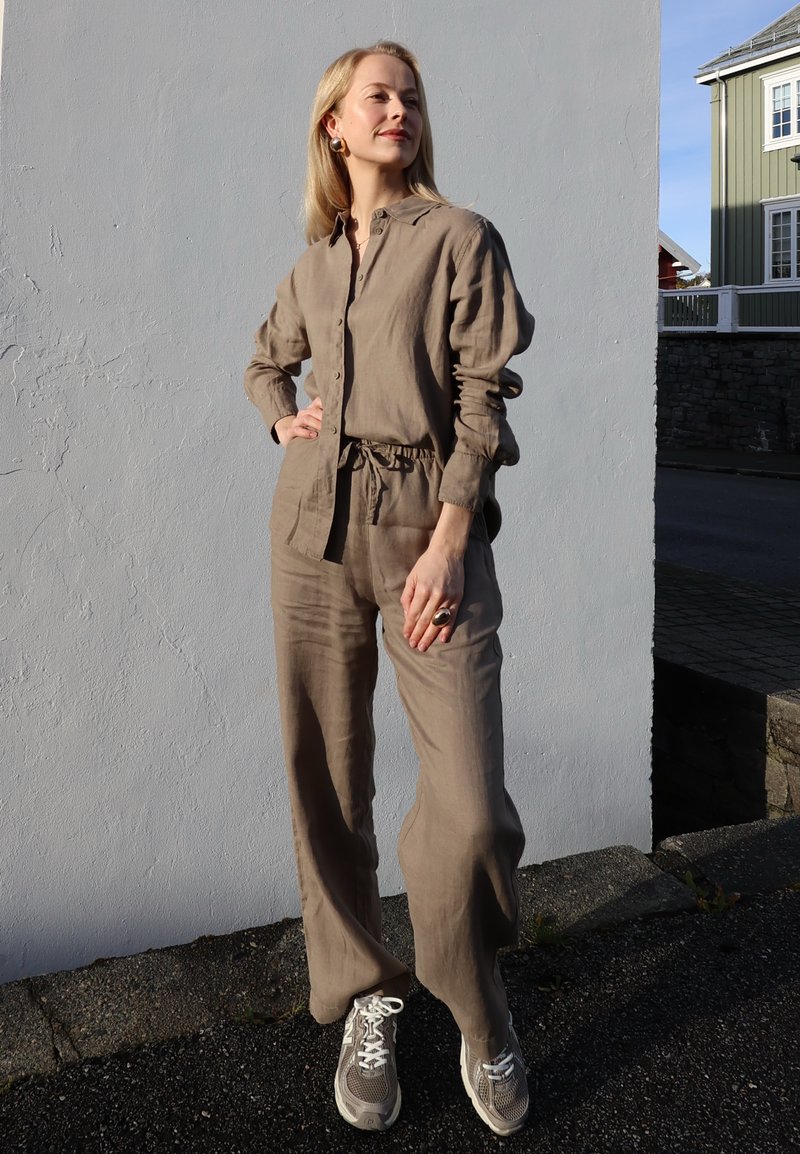 Lysebrun hørskjorte med knaplukning, kombineret med matchende bukser med vidde ben. Afslappede grå sneakers med hvide detaljer. Minimale accessories.