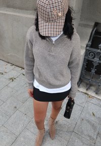 Bež pleteni zip-sveter preko bijele majice, uparen s crnom mini suknjom i bež čizmama s patom. Crna torba.