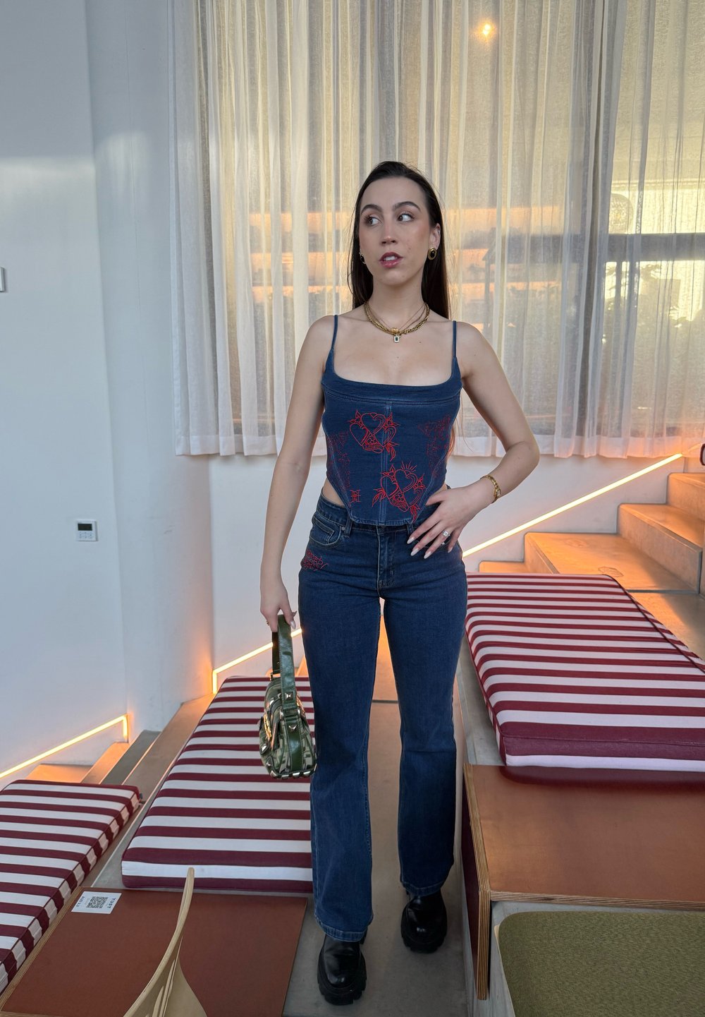 Blå kort tanktopp med rød blomsterbroderi, kombinert med høy midje blå jeans og svarte platåsko. Holder en grønn håndveske.