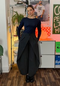 Pantalones de pierna ancha a rayas negras con un panel frontal, combinados con una blusa ajustada de manga larga azul marino y zapatos de plataforma negros.