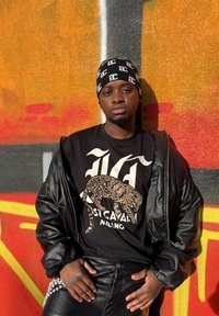 Sort læder bomberjakke over en sort T-shirt med grafik med leoparddesign. Slanke sorte bukser med en perlekæde som detalje ved taljen.