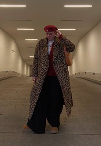 Καμπαρντίνα με λεοπάρ πατίνα και μεγάλους γιακάδες, συνδυασμένη με μπορντώ τοπ και μαύρο παντελόνι φαρδύ. Κόκκινο μπερέ και καμία τσάντα ολοκληρώνουν την εμφάνιση.