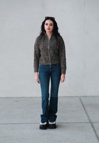 Veste marron en maille avec fermeture éclair, coupe ajustée. Jean bleu foncé évasé, retroussé en bas. Chaussures à plateforme noires épaisses avec accents blancs.