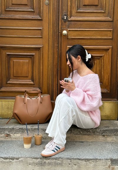 Suéter de punto rosa claro, pantalones blancos de pierna ancha, bolso de cuero marrón, dos cafés helados con popotes y zapatillas grises con rayas azules.