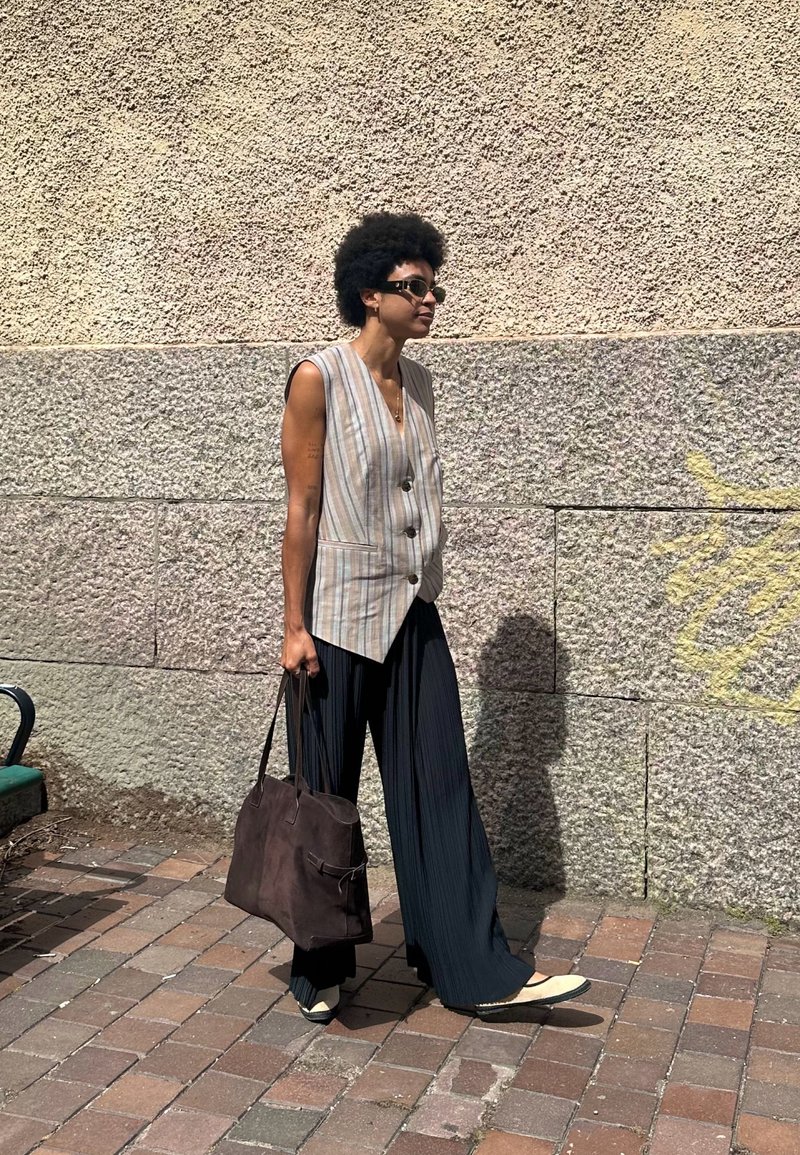 Ριγέ αμάνικο γιλέκο με δύο κουμπιά, συνδυασμένο με φαρδιά, πλισέ μαύρα παντελόνια. Μια καφέ τσάντα και ελαφριά, επίπεδη παπούτσια ολοκληρώνουν την εμφάνιση.