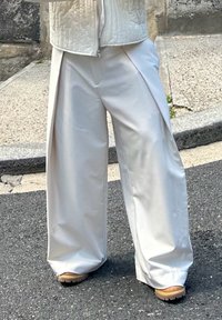 Pantaloni albi, cu croi larg, dintr-un material neted, mat, cu pliseuri frontale. Asortați cu pantofi cu platformă bej, având tălpi texturate.