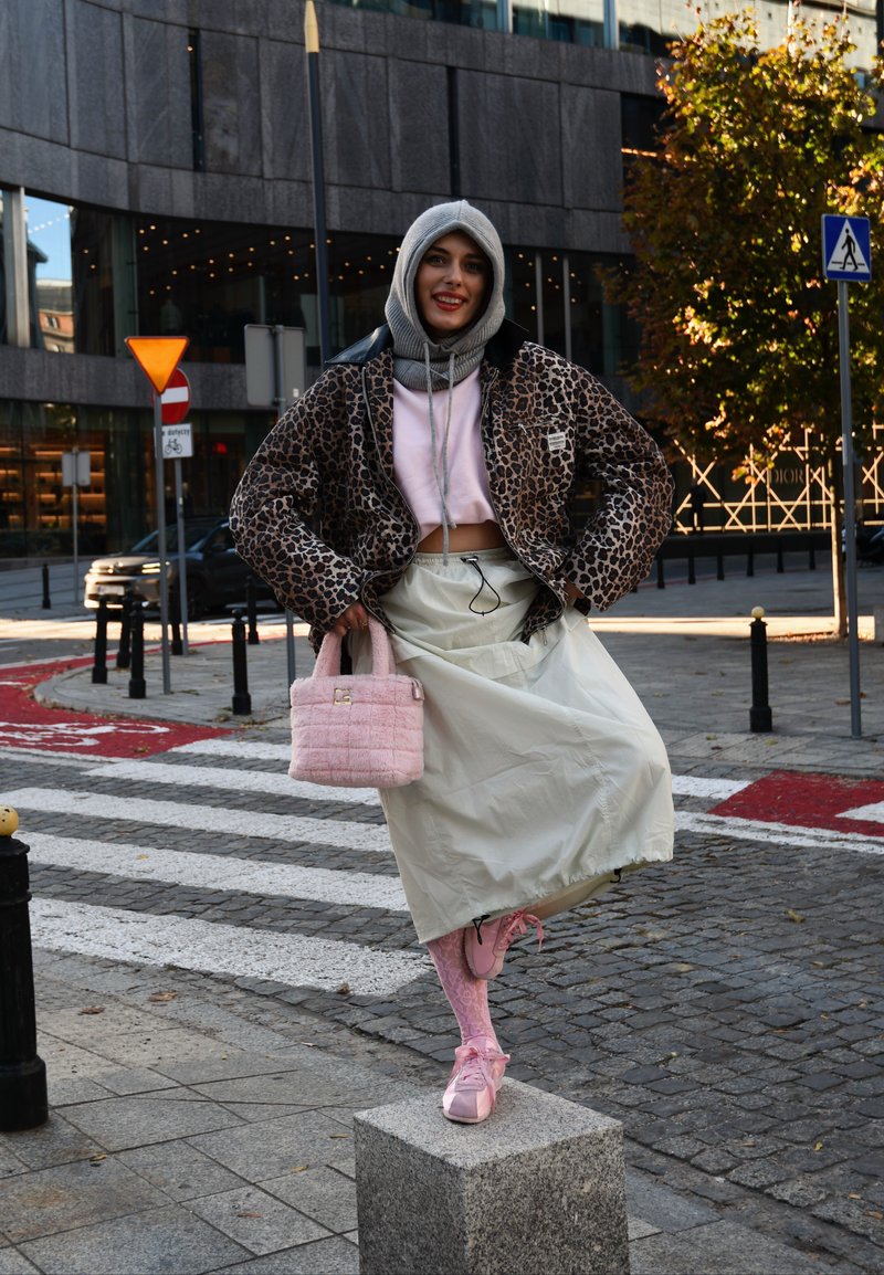 Μπλούζα cropped με λεοπάρ σχέδιο, ροζ crop top, μπεζ φούστα, ροζ пухυ χέρι, ροζ κάλτσες και ροζ παπούτσια σε έναν δρόμο με σχέδιο στο πλακόστρωτο.