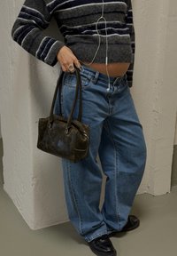 Pull rayé gris, jean bleu coupe décontractée et petit sac à main en cuir vert foncé. Écouteurs visibles, avec des textures lisses partout.