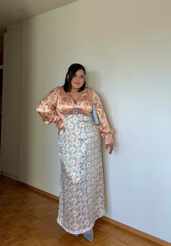 Larga falda floral con estampados en azul, rosa y blanco, combinada con una blusa brillante de manga larga rosa con escote en V.