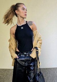 Μαύρο ολόσωμο μαγιό με λευκό λογότυπο Adidas, συνδυασμένο με ταμπά μπουφάν και μαύρο δερμάτινο παντελόνι πλατύ. Κολιέ με χάντρες και τσάντα χιαστί.