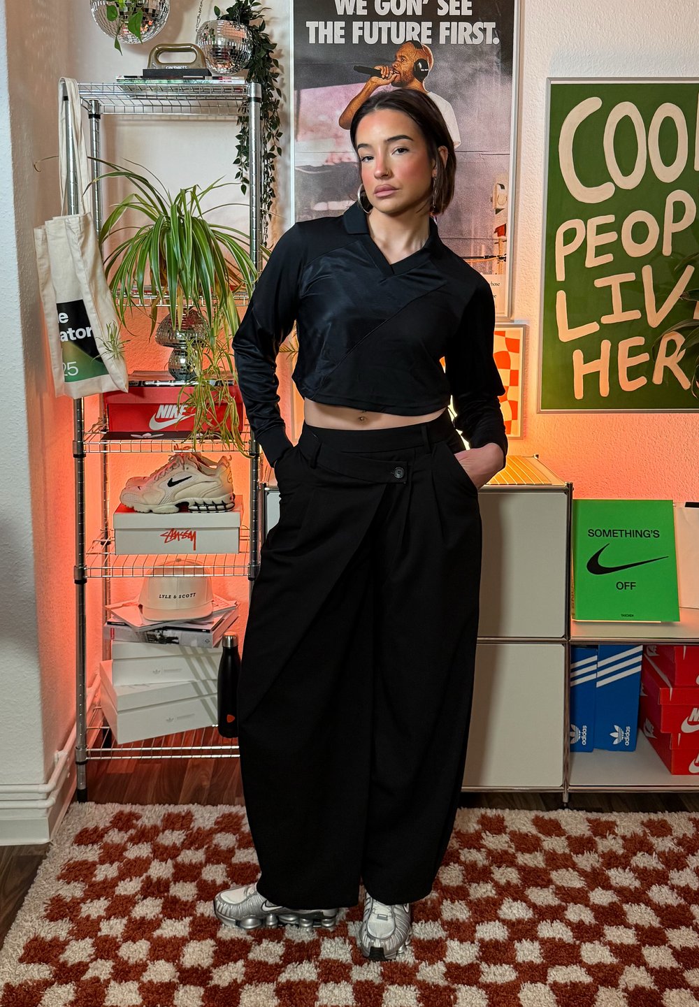 Haut noir à manches longues raccourci avec un design cache-cœur, associé à un pantalon noir ample. Chaussures composées de baskets gris clair avec une semelle texturée.