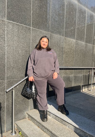 Conjunto de salón gris hecho de tela suave, que incluye una sudadera de corte holgado y pantalones. Los accesorios incluyen un bolso negro con tachuelas y botas negras gruesas.