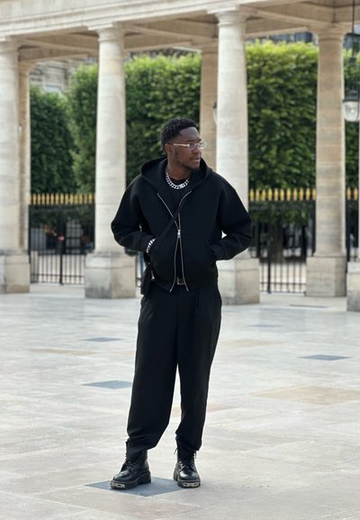 Sudadera negra con cremallera y acabado texturizado, combinada con pantalones negros de corte holgado y botas negras con suelas gruesas.