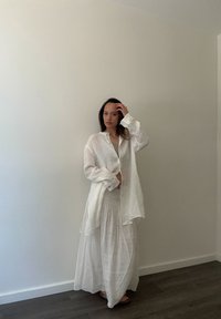 Conjunto de camisa de lino blanco y falda maxi con un ajuste relajado y tejido texturizado. La camisa tiene un dobladillo largo y detalles de botones.