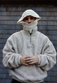 Pull polaire beige avec col montant et fermeture éclair. Bonnet à torsades avec large bord et protection pour la nuque. Orné d'un logo.