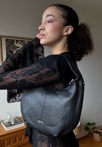 Sac à main en cuir noir avec un design courbé, présentant un détail de couture subtil, des accents métalliques, et une texture douce. Porté à l'épaule.