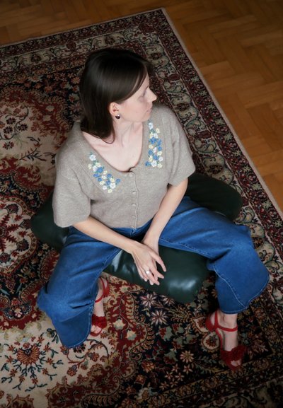 Cárdigan de punto beige con bordado floral, mangas cortas y cierre de botones; combinado con pantalones vaqueros de pierna ancha azules y sandalias de tacón rojas.