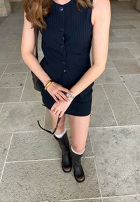Marineblauw gestreept vest met vijf knopen, aansluitende mini-jurk en kniehoge zwarte leren laarzen met gespsieraden. Minimale accessoires.