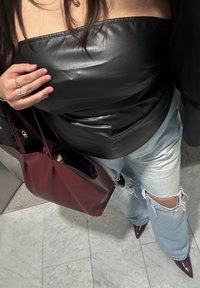 Top in eco-pelle nera con design aderente, abbinato a jeans chiari strappati e a una borsa a tracolla bordeaux. Le scarpe col tacco a punta bordeaux completano l'outfit.