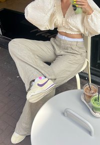 Cream textured cropped blouse, light beige wide-leg trousers, and fuzzy white trainers with purple accents. Two drinks on a table.