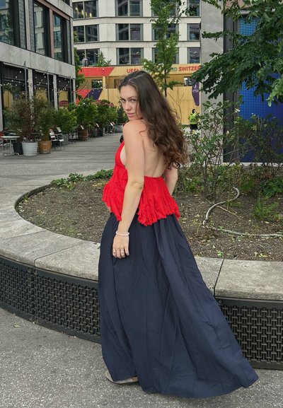 Vestido maxi con un corpiño texturizado rojo y una falda fluida azul marino. La espalda está descubierta y se combina con accesorios sencillos, de pie al aire libre.