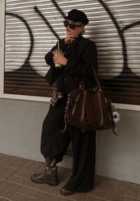 Fekete, túlméretezett blézer kockás inggel, széles fekete nadrág, barna bőr csizma, és egy nagy barna táska. Zöld ital a kézben.