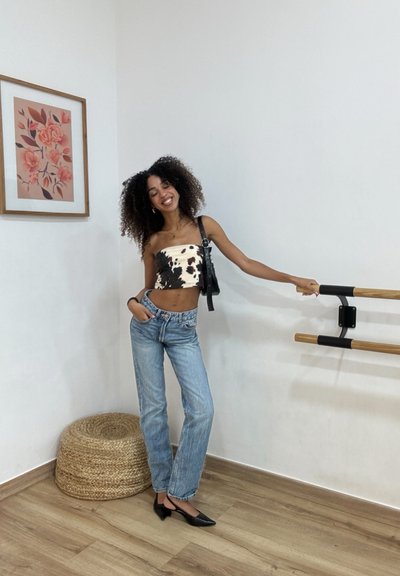 Top corto sin tirantes en blanco y negro combinado con jeans rectos de color azul claro, tacones negros de punta y un pequeño bolso negro.