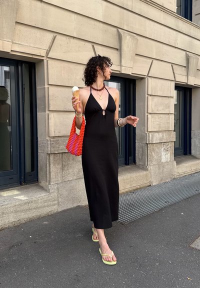 Vestido maxi negro sin mangas con un escote en forma de llave en la parte delantera, acompañado de un vibrante bolso texturizado en colores naranja y rosa. Sosteniendo un cono de helado. Chanclas verdes.