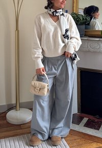 Pull crème surdimensionné, pantalon large bleu clair, sac à main beige et pantoufles camel ; accent avec une écharpe noire et blanche à motifs.