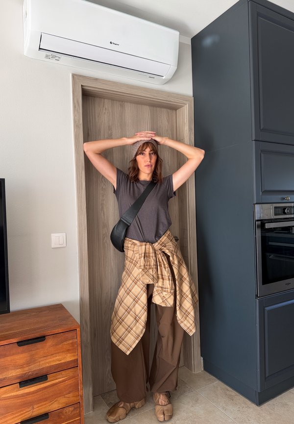 Una mujer está de pie en la entrada de una cocina con las manos en la cabeza, debajo de un aire acondicionado instalado en la pared.