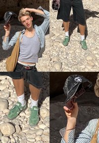 Νέος άνδρας με ριγέ πουκάμισο και γκρι αμάνικο κρατάει μαύρο καπέλο, στέκεται σε βραχώδες έδαφος φορώντας πράσινα αθλητικά παπούτσια και μαύρα σορτς.