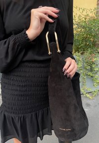 Μαύρη σουέτ τσάντα χειρός με στρογγυλό σχήμα, χρυσά αξεσουάρ στη λουρίδα, με το "MICHAEL KORS" ανάγλυφο σε χρυσό. Ορατές υφασμάτινες λεπτομέρειες.