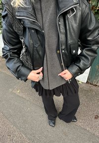 Čierna kožená bunda, sivý rebrovaný sveter, čierne šaty s volánmi a čierne široké nohavice. Doplnky zahŕňajú retiazkovú kabelku a prstene.