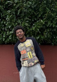 Pull multicolore avec texte ludique et motifs, comprenant un tissu côtelé noir sur les manches. Pantalon de survêtement gris, posé devant un fond vert.